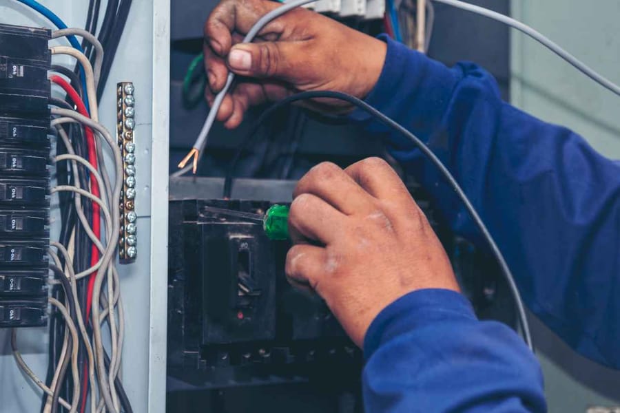 Electrician checking electrical panel and doing maintenance on the panel. His hands are fixing the breaker and repairing the circuit.