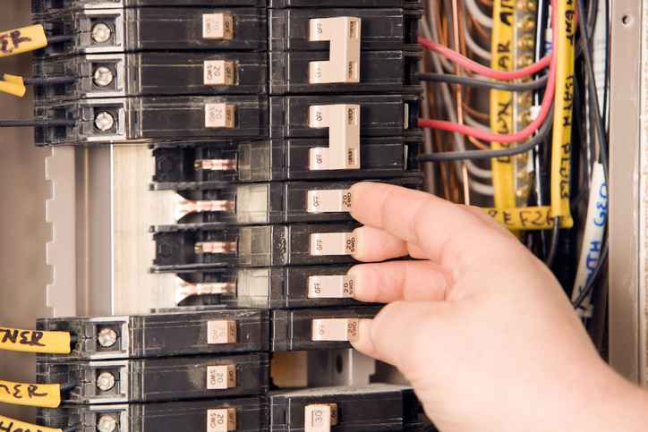 Electrician's hands turning on circuit breakers on electrical panel